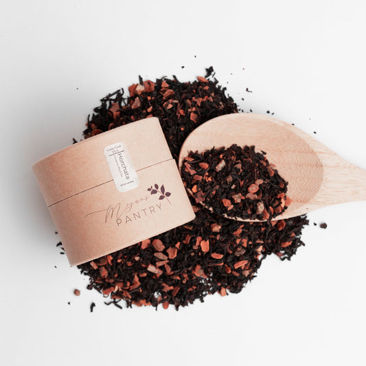 Tea leaves spilling from a wooden scoop into a cardboard container on a white background