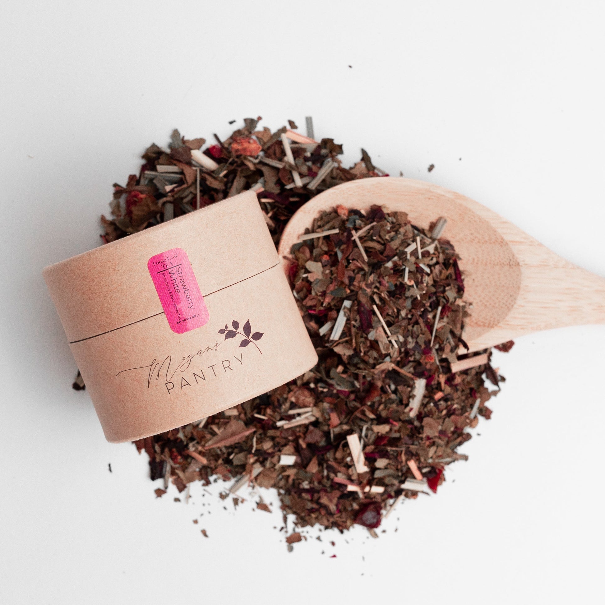Wooden scoop filled with dried herbs or spices next to a small cardboard container on a white background