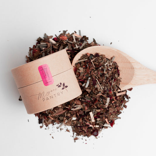 Wooden scoop filled with dried herbs or spices next to a small cardboard container on a white background